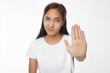 Confident or displeased young brunette Chinese female making stop gesture, holding open palm in front of her, demanding not to come close to her. Stay away from me. Selective focus on woman's hand