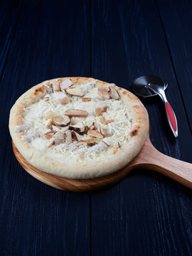 Frozen pizza with porcini and truffle, on a wooden board, set on a dark blue background