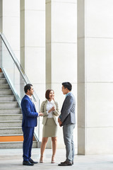 Multiethnic group of business people standing and talking to each other before meeting at office corridor