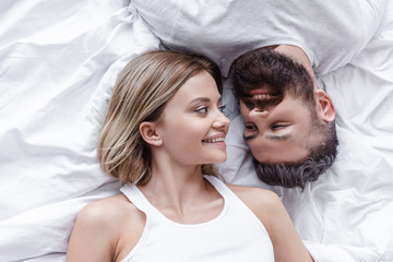 Fototapeta na wymiar young couple in love lying head to head and looking to each other on white blanket