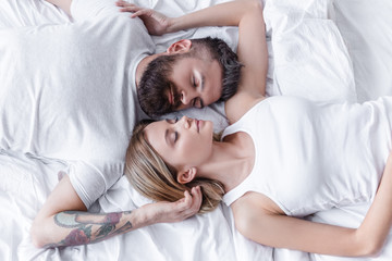 pretty couple in love lying head to head and sleeping in white bed