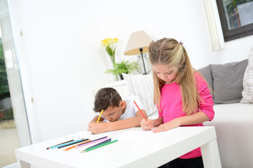 two beautiful young kids boy and girl drawing on a white paper with color pencil