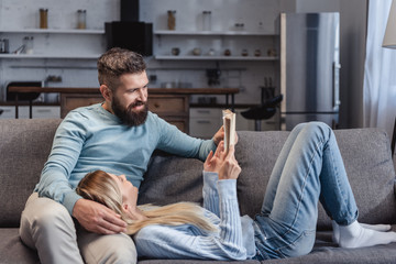 Wife holding book and lying on knees of husband