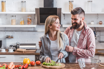Cheerful and smiling couple preparing dinner in kitchen