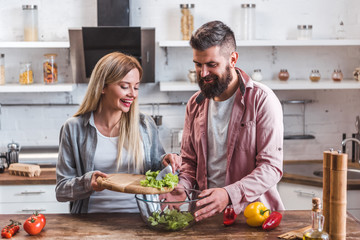 Cheerful couple adding salad leaves in bowl