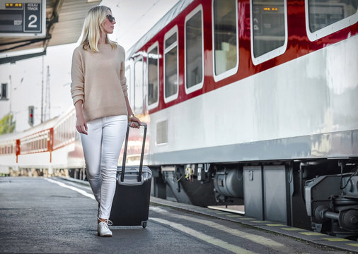Blonde woman with her luggage go near the red train on the peron