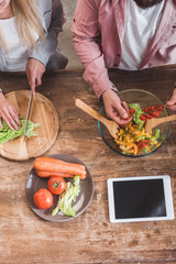 cropped view of couple cooking vegetable salad with digital tablet at wooden table