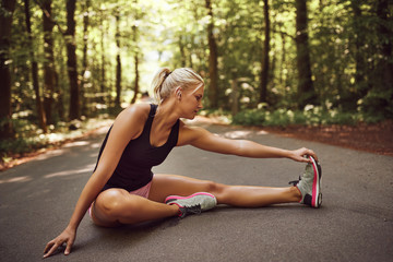 Fit young woman stretching her legs before a forest run