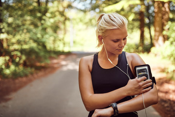 Fit woman queueing up her playlist before a countryside run