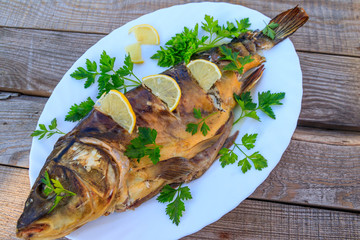 Baked carp fish with lemon and parsley on wooden table
