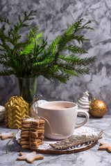 Obraz na płótnie Canvas A white cup with hot cocoa with marshmallow stands on a gray table among white and gold Christmas ornaments and fir branches