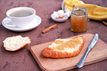 Breakfast: a cup of coffee, fresh croissant and orange jam