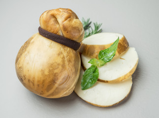 Traditional Italian smoked Scamorza cheese with herbs on gray background. © volff