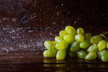 Several varieties of grapes on a wooden background with splashes of water. Fresh fruit concept, new crop