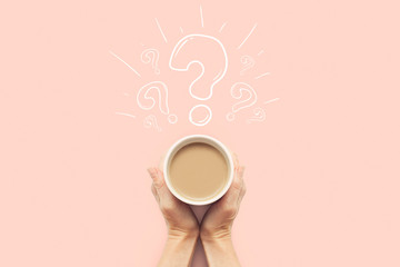 A hand is holding a cup with hot coffee on a pink background. Question mark. Breakfast concept with coffee or tea. Good morning, night, insomnia. Flat lay, top view