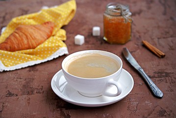 Breakfast: a cup of coffee, fresh croissant and orange jam