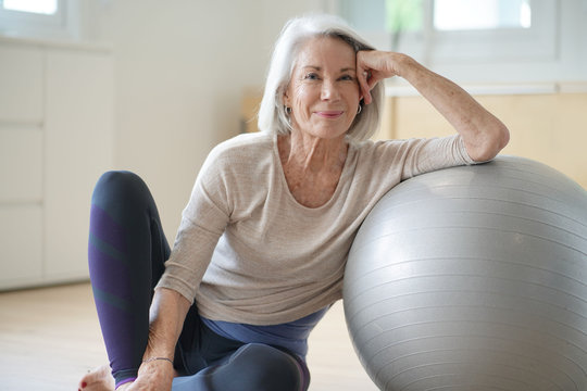  Smiling elderly woman resting on a swiss ball at home