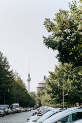 Beautiful view of the TV tower among the trees and the street with parking in Berlin in Germany.