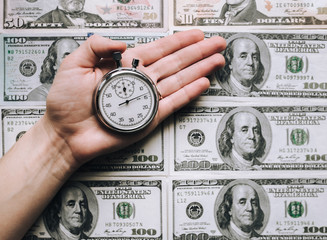 Usurer, credit concept. Time for quick money. Woman's hand holding a grey stopwatch over dollars...