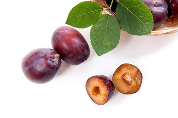 Yellow wooden basket with ripe plums, whole and half ripe plums isolated on a white background..