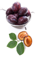 Steel colander with ripe plums, whole and half ripe plums with leaf isolated on a white background..
