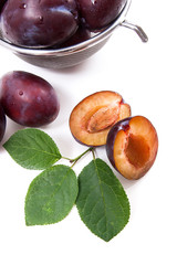 Steel colander with ripe plums, whole and half ripe plums with leaf isolated on a white background..