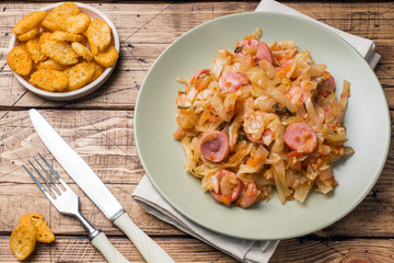Stewed cabbage with sausages in a plate on the table. Selective focus.