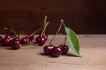 Red sweet cherry with green leaf on wooden background.