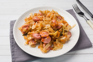 Stewed cabbage with sausages in a plate on the table. Selective focus.