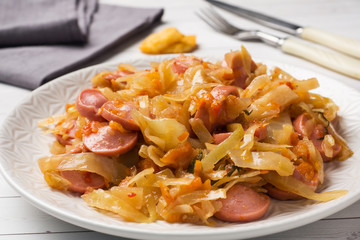 Stewed cabbage with sausages in a plate on the table. Selective focus.