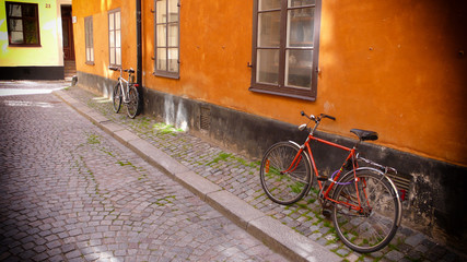 Fototapeta na wymiar Red Bicycle on an Orange Wall on a cobblestone street in Stockholm, Sweden