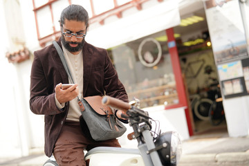 Hipster guy with electric vintage style bike using smartphone