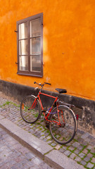 Fototapeta na wymiar Red Bicycle on an Orange Wall on a cobblestone street in Stockholm, Sweden