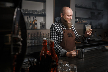 Brutal young barista in an apron tasting coffee at the bar in a modern cafe