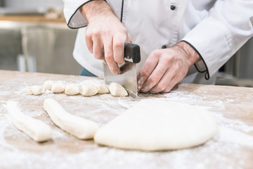 close up of chefs hands separating dough with cutter on wooden table