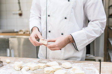 Cropped view of baker in chefs uniform cooking dough on wooden table