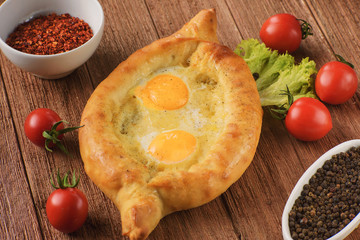 fresh and hot Ajarian khachapuri on a wooden table with lettuce, tomatoes and spices