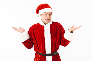 Fototapeta na wymiar Portrait of surprised man 30s in santa claus costume and red hat throwing up hands, isolated over white background in studio
