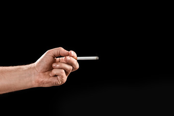 Male hand holding a cigarette, close-up, black background. The concept of smoking kills, nekatin is poison, nicotine addiction. Copy space.