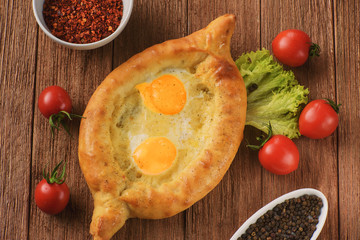 fresh and hot Ajarian khachapuri on a wooden table with lettuce, tomatoes and spices