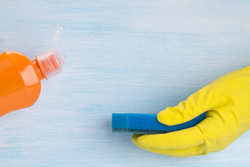 on a blue background, a hand in a protective glove, holding a foam sponge for cleaning surfaces and a bottle