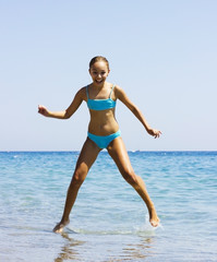 Fototapeta premium Young pretty smiling girl in blue swimsuit jumping into the sea