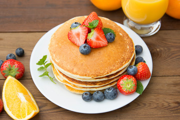 Homemade american pancake with fresh blueberries, strawberries and orange juice. Wooden rustic background.