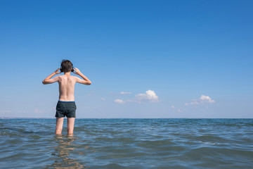 Happy cheerful teen boy on the beach with the headphones running on the wave of the sea  background. Concept