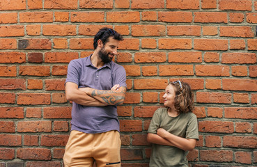Content son and father leaning against a brick wall outside