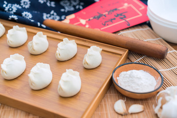 Dumplings, flour, rolling sticks, red envelopes on the wooden table