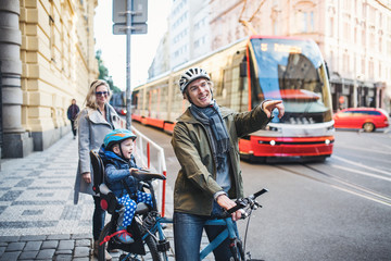 A small toddler boy sitting in bicycle seat with young parents outdoors in city.