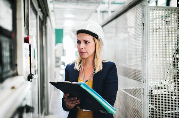 A portrait of an industrial woman engineer in a factory, writing.