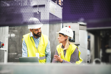A portrait of an industrial man and woman engineer with laptop in a factory, working.