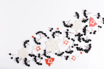 Christmas composition. Black chokeberry berries, white knitted snowballs and white-red Christmas trees on white background. Flat lay, top view, copy space